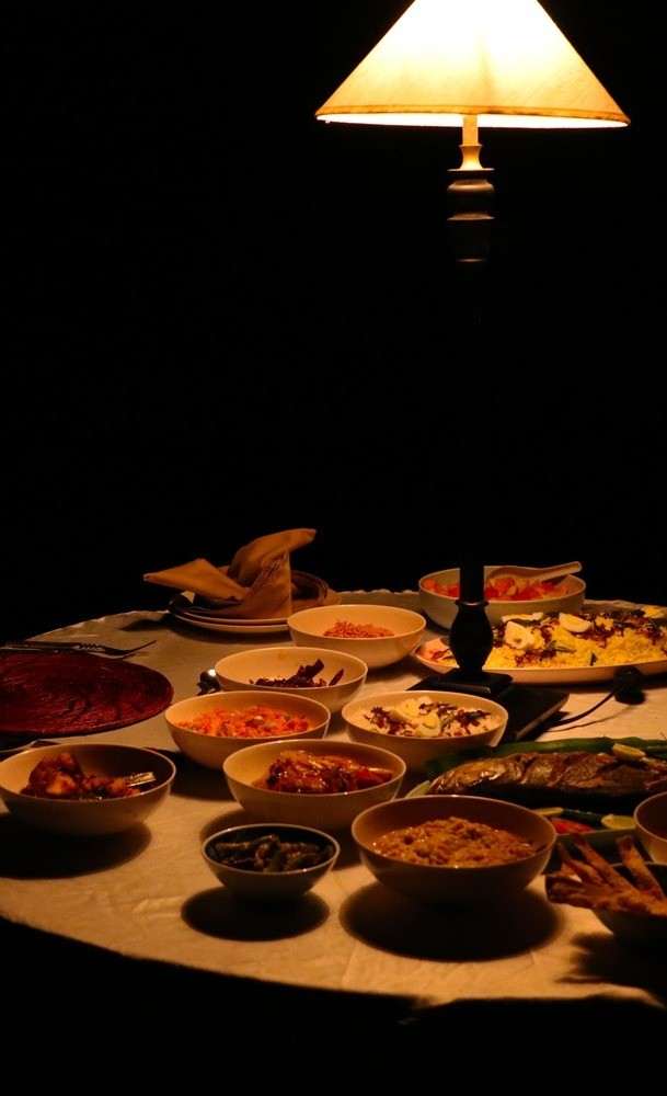 A round table at night laid with many small dishes of Sri Lankan food under a lamp.