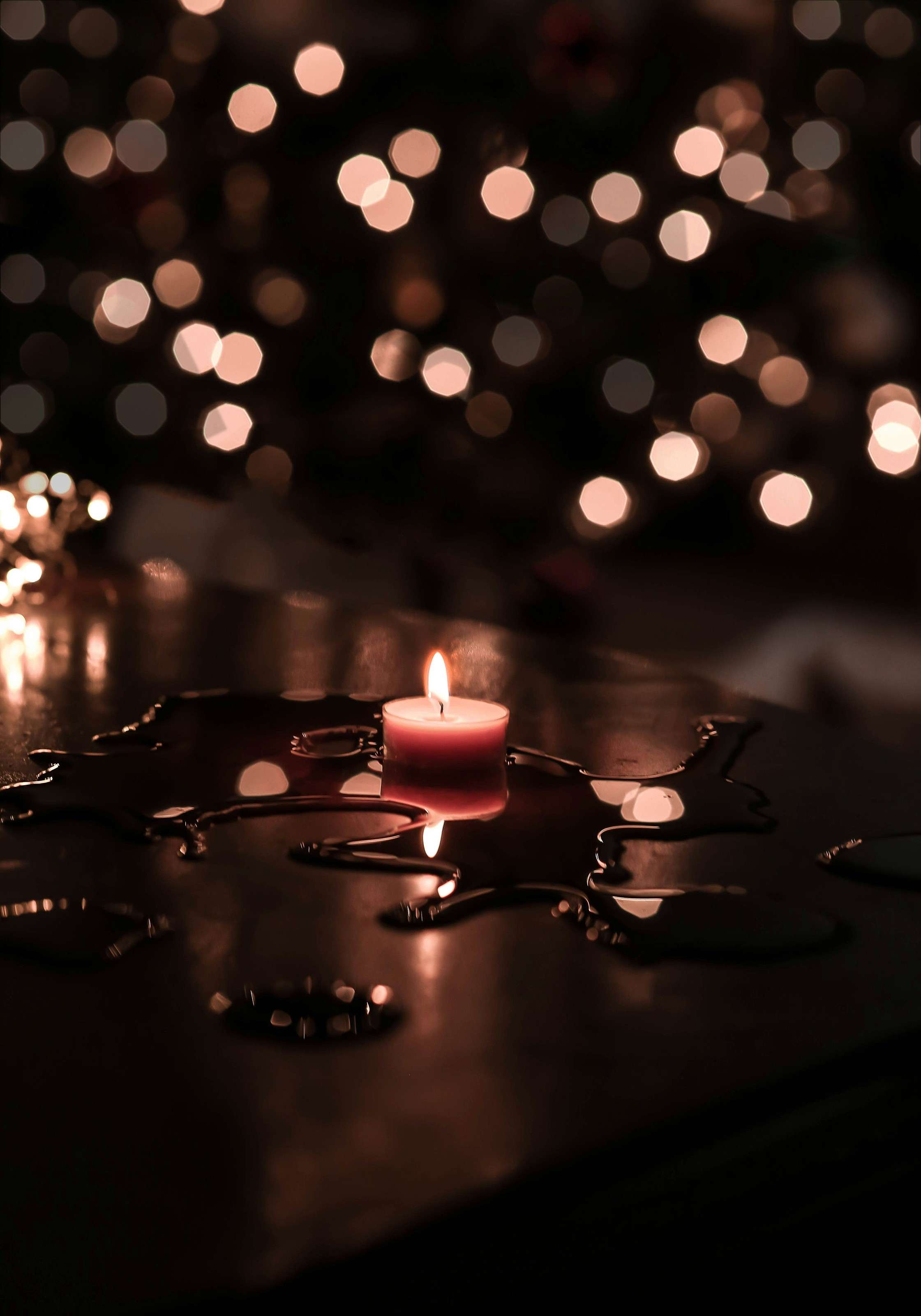 A single candle burning on a dark table at night, with blurred lights behind.