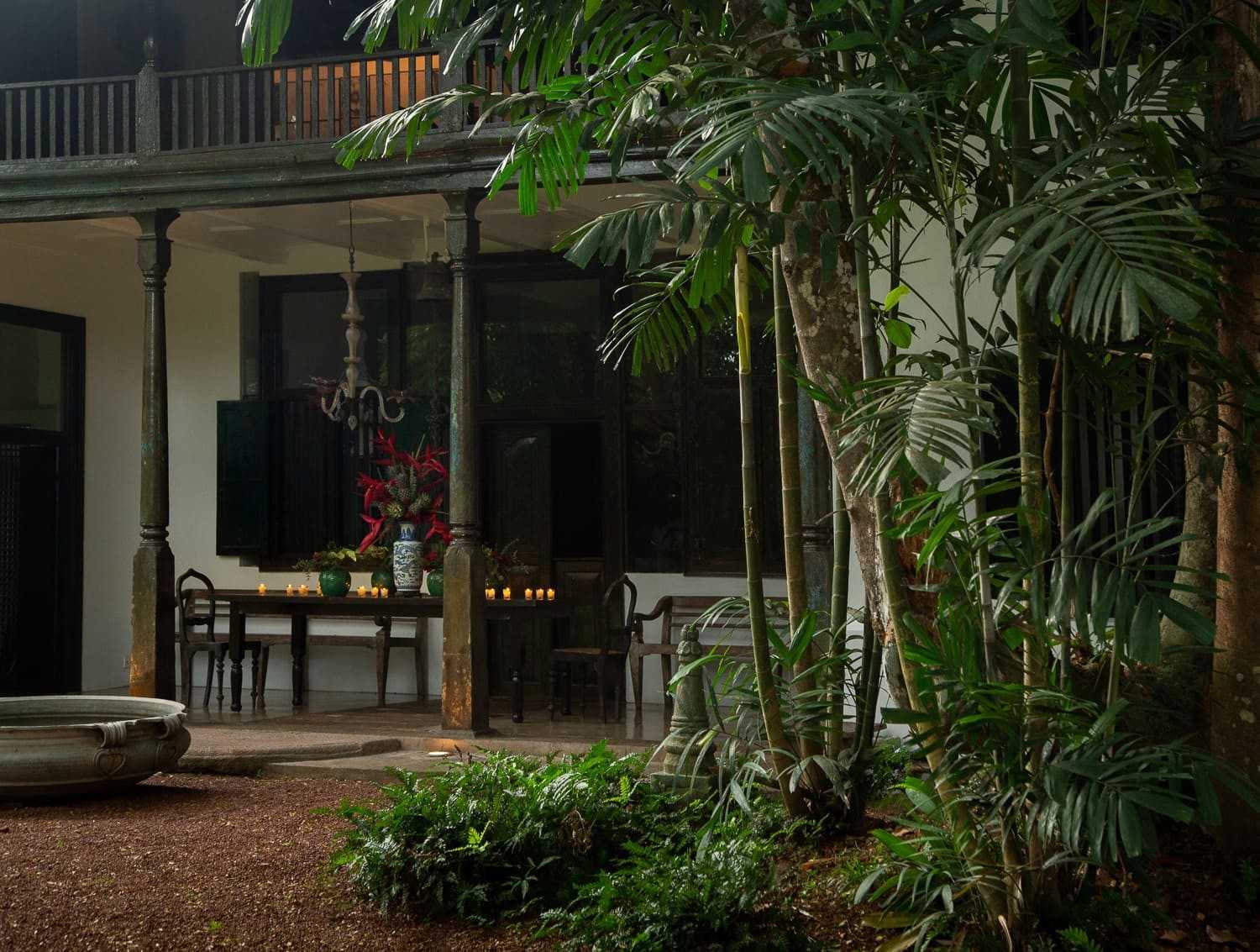 The villa's veranda, dark timber posts under a tiled roof, and a garden of palms and ferns in front.