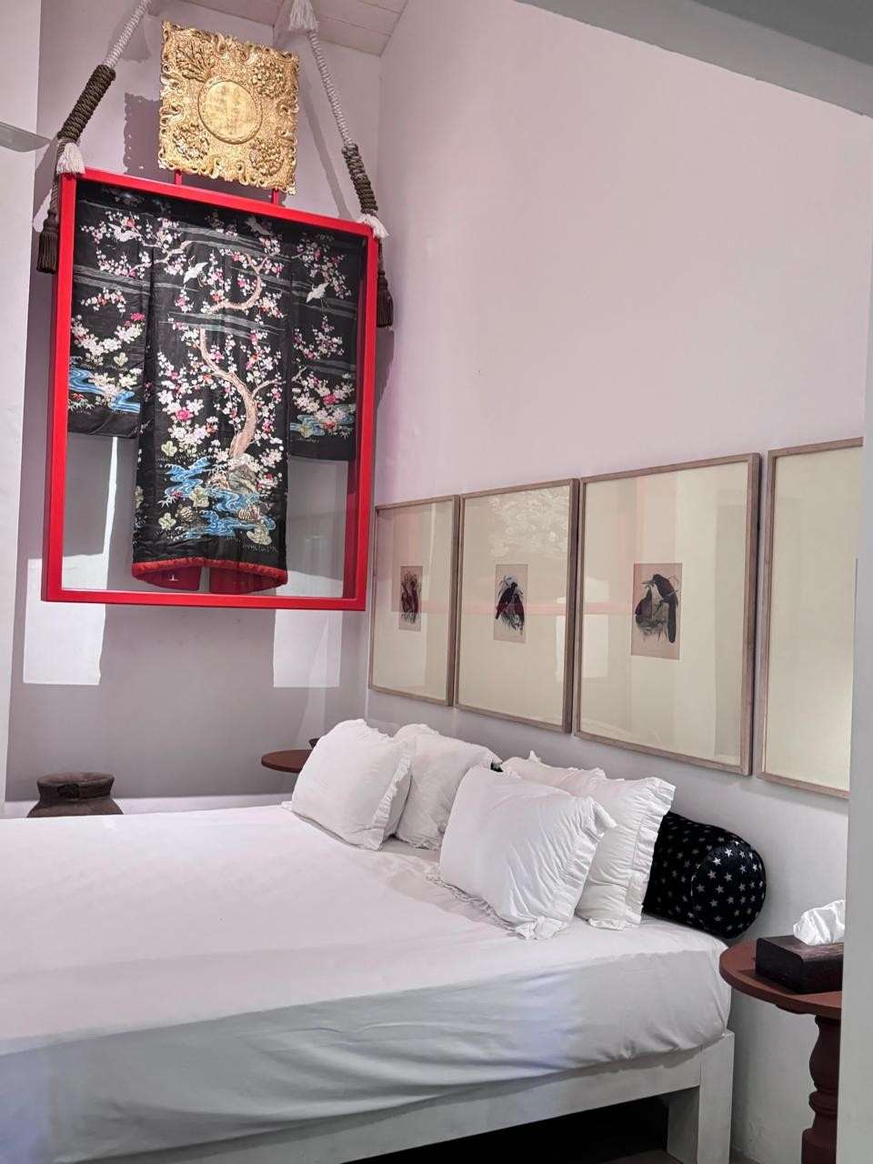 The Poolside Suite: a white bed beneath an embroidered kimono framed in red, with framed prints along the wall.